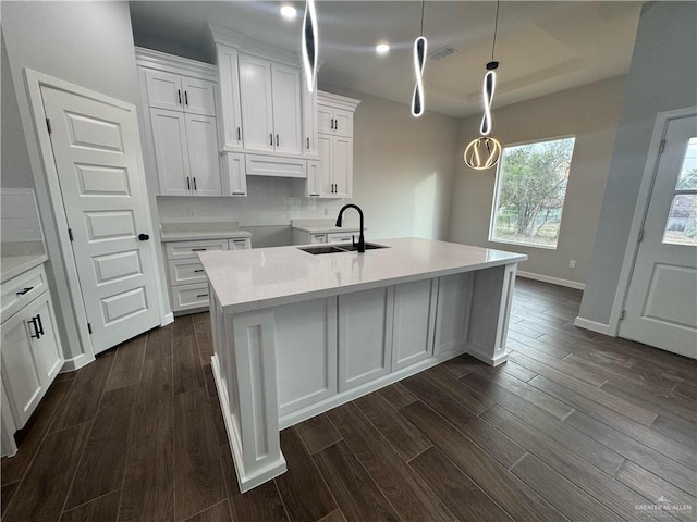 kitchen with dark wood finished floors, an island with sink, light countertops, white cabinetry, and a sink