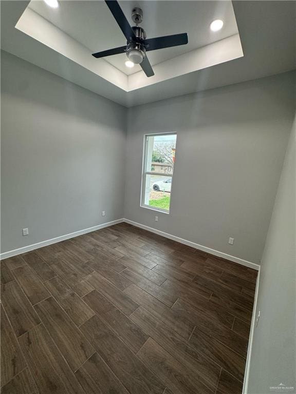 empty room featuring baseboards, dark wood finished floors, recessed lighting, ceiling fan, and a raised ceiling