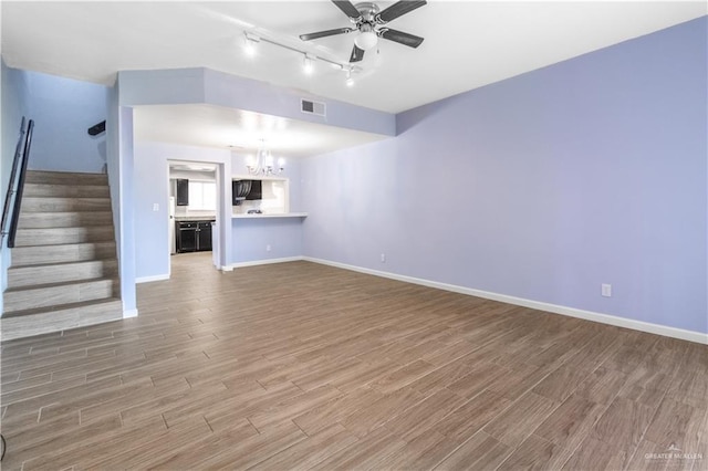 unfurnished living room featuring ceiling fan with notable chandelier, wood finished floors, visible vents, and stairs