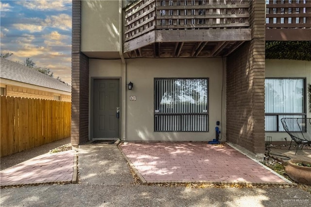 property entrance featuring brick siding, fence, and stucco siding