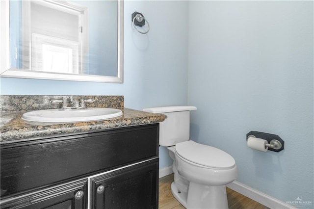 half bath featuring toilet, baseboards, wood finished floors, and vanity