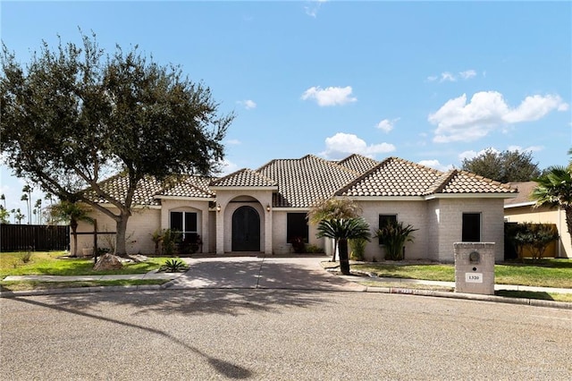 mediterranean / spanish-style home featuring driveway, fence, and a tiled roof