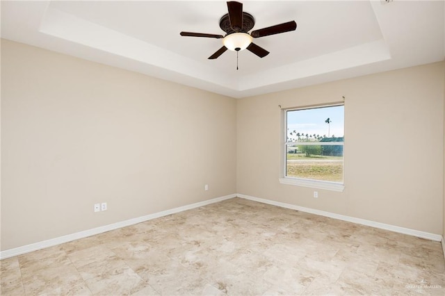 empty room featuring a tray ceiling, a ceiling fan, and baseboards