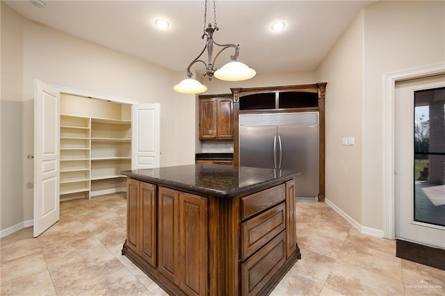 kitchen with a kitchen island, baseboards, stainless steel built in fridge, dark stone counters, and pendant lighting