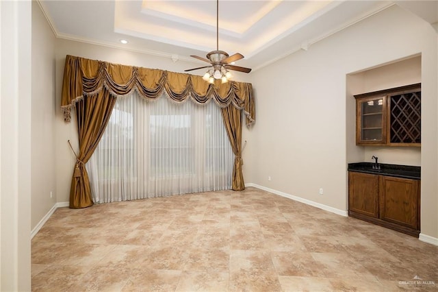 unfurnished dining area with baseboards, ceiling fan, a raised ceiling, and wet bar