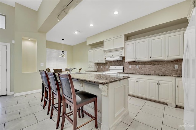 kitchen with decorative light fixtures, white cabinetry, white appliances, and an island with sink