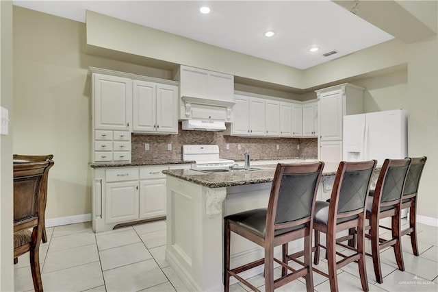 kitchen with tasteful backsplash, a kitchen island with sink, white cabinets, and white appliances