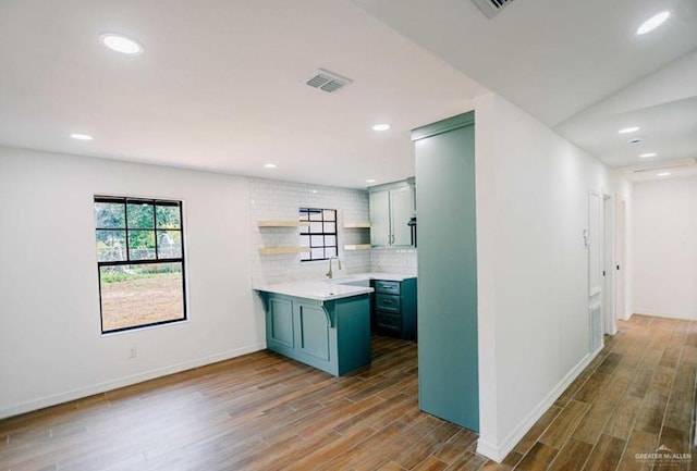 kitchen featuring kitchen peninsula, wood-type flooring, sink, and tasteful backsplash