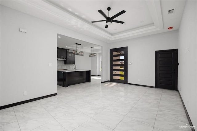 unfurnished living room with ceiling fan, sink, and a raised ceiling