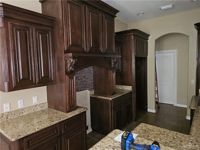 kitchen featuring dark tile patterned flooring, arched walkways, light stone counters, and dark brown cabinets