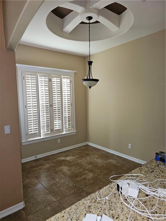 unfurnished dining area with baseboards, a ceiling fan, and a tray ceiling