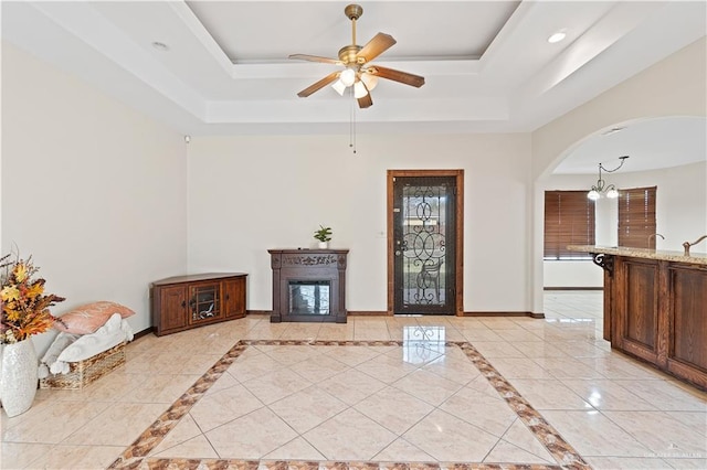 foyer with arched walkways, a glass covered fireplace, a raised ceiling, and baseboards