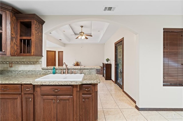 kitchen featuring light tile patterned floors, a sink, visible vents, decorative backsplash, and a tray ceiling