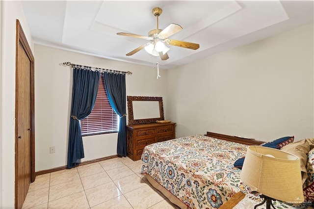 bedroom featuring light tile patterned floors, ceiling fan, a tray ceiling, and baseboards