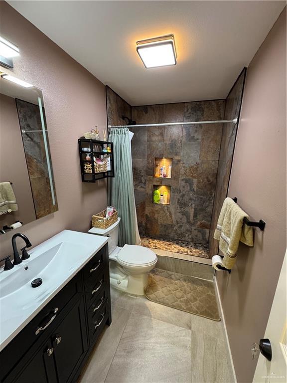 bathroom featuring tiled shower, vanity, and toilet