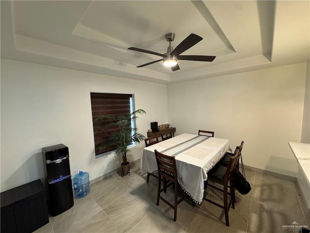 dining area featuring a tray ceiling, a ceiling fan, and baseboards