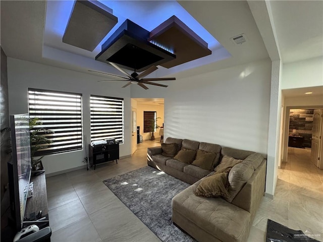 living room featuring visible vents, a tray ceiling, ceiling fan, and baseboards