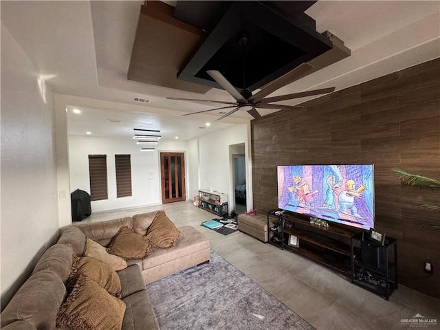 living area with wood walls, a raised ceiling, visible vents, and recessed lighting