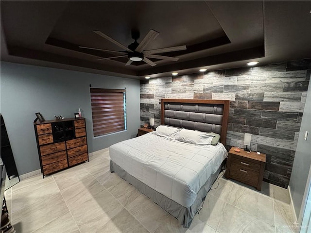 bedroom featuring a ceiling fan, a tray ceiling, an accent wall, and baseboards