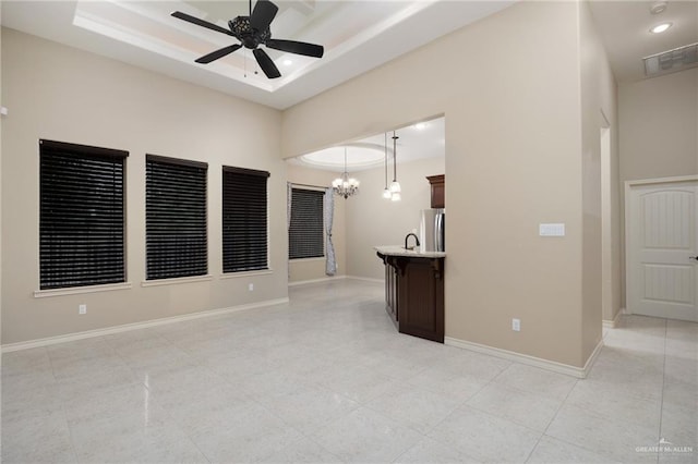 empty room featuring ceiling fan with notable chandelier, a raised ceiling, and sink