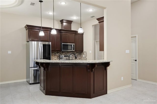 kitchen featuring a breakfast bar, light stone countertops, decorative light fixtures, dark brown cabinets, and appliances with stainless steel finishes