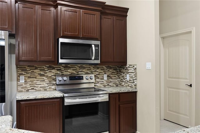 kitchen featuring light stone countertops, dark brown cabinets, backsplash, and stainless steel appliances