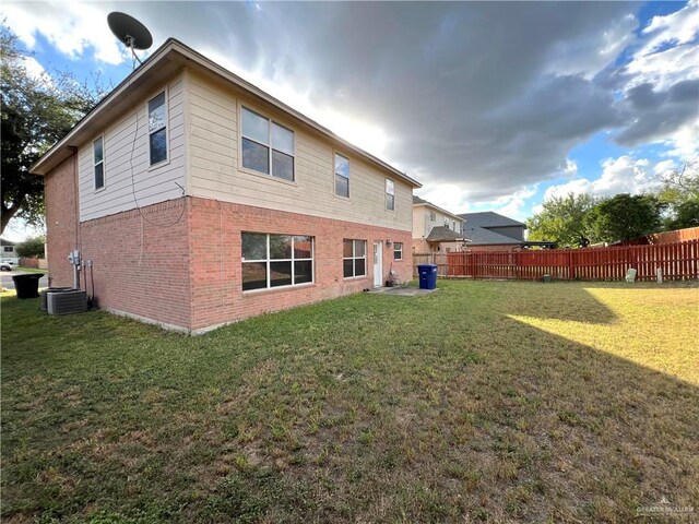 rear view of property with central AC unit and a lawn