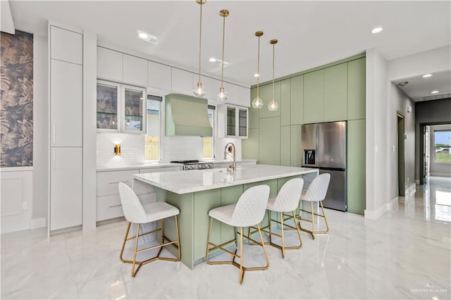 kitchen with premium range hood, stainless steel appliances, a kitchen island with sink, pendant lighting, and white cabinets