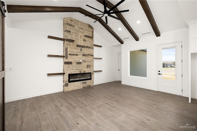 unfurnished living room with beam ceiling, a stone fireplace, ceiling fan, and hardwood / wood-style flooring