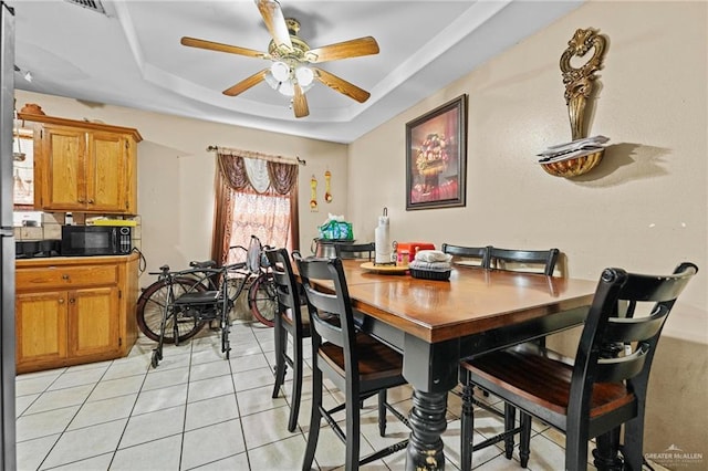 dining area with a raised ceiling, light tile patterned flooring, and ceiling fan