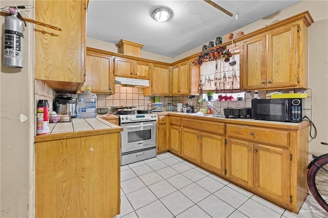 kitchen with sink, light tile patterned floors, backsplash, stainless steel range, and tile counters