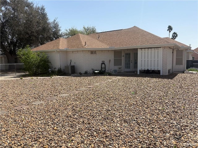 rear view of house featuring brick siding, french doors, central AC, and roof with shingles