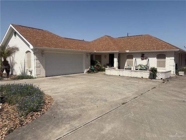 ranch-style home featuring brick siding, an attached garage, driveway, and a shingled roof