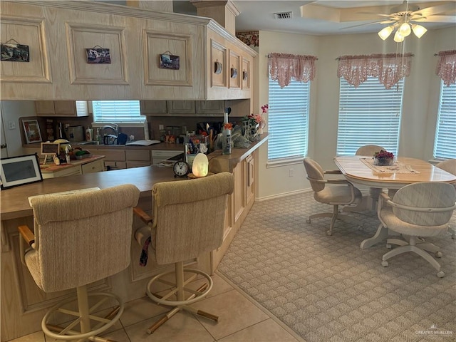 kitchen featuring visible vents, baseboards, ceiling fan, dishwashing machine, and a kitchen breakfast bar
