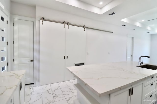 kitchen featuring sink, white cabinets, a kitchen island with sink, light stone counters, and a barn door