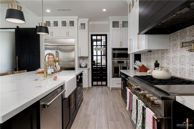 4825 Estancia Pkwy, Mcallen, TX 78504 - kitchen featuring high end appliances, wall chimney exhaust hood, a barn door, white cabinets, and recessed lighting