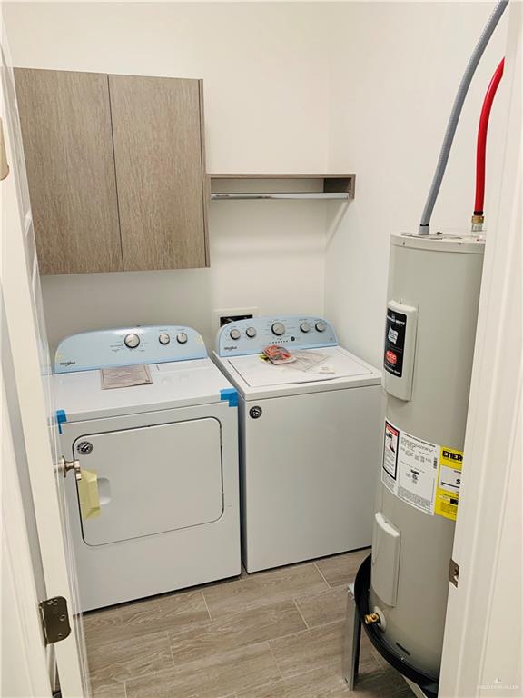 laundry area with electric water heater, washer and clothes dryer, cabinets, and light hardwood / wood-style flooring