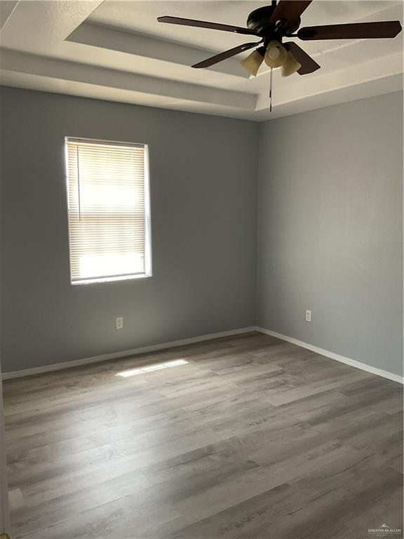 spare room featuring a tray ceiling, wood finished floors, and baseboards