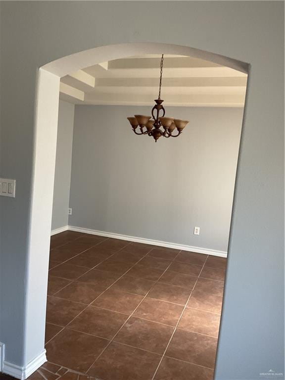 spare room featuring baseboards, a chandelier, arched walkways, a raised ceiling, and dark tile patterned flooring