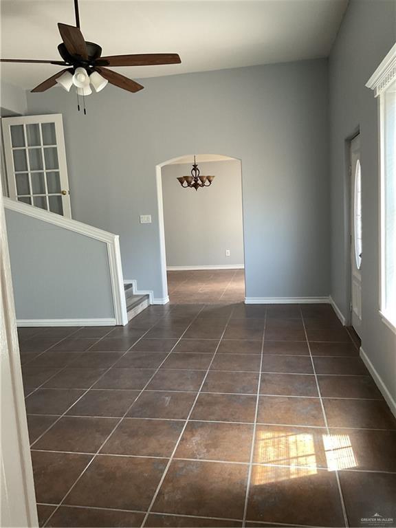 unfurnished room featuring stairway, baseboards, arched walkways, tile patterned flooring, and ceiling fan with notable chandelier