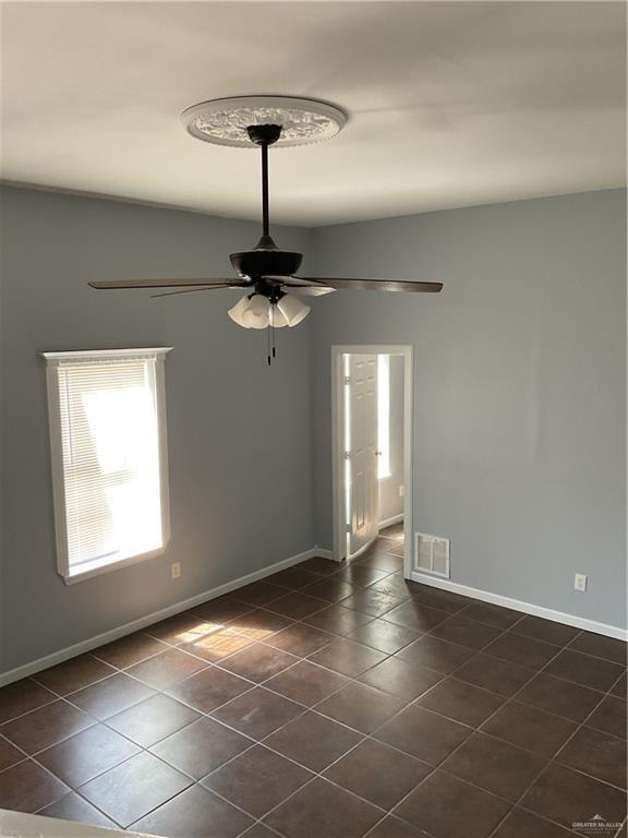 unfurnished room featuring dark tile patterned floors, visible vents, baseboards, and ceiling fan