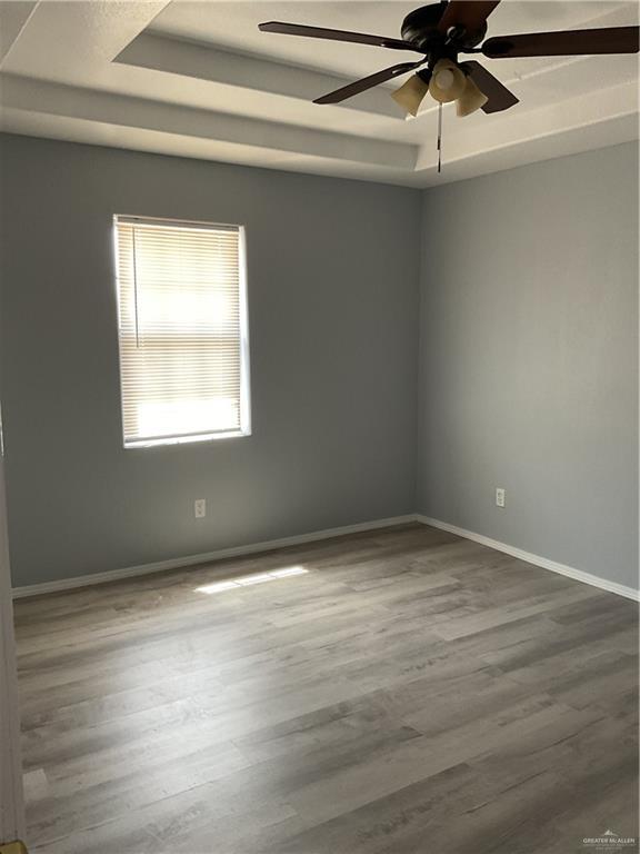 spare room featuring a raised ceiling, wood finished floors, and baseboards