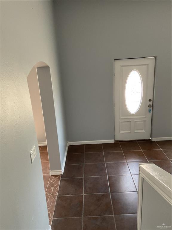 entryway featuring baseboards, arched walkways, and dark tile patterned floors