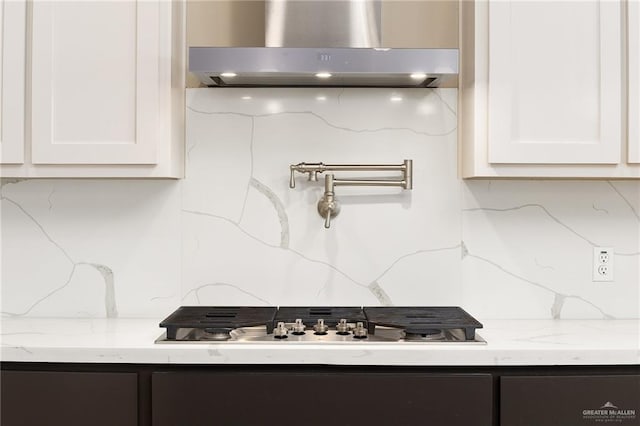 kitchen featuring white cabinetry, wall chimney exhaust hood, light stone countertops, and tasteful backsplash