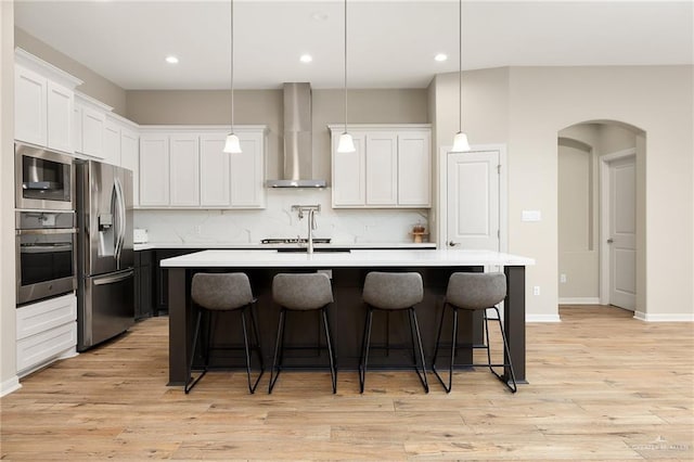 kitchen featuring pendant lighting, wall chimney range hood, a center island with sink, and appliances with stainless steel finishes