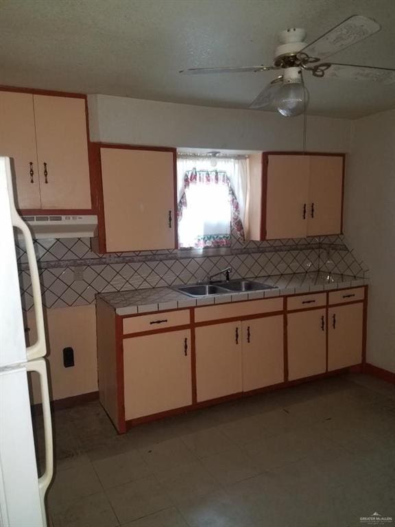 kitchen with decorative backsplash, white refrigerator, sink, and ceiling fan