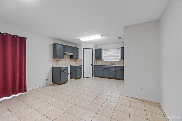 3017 Paradise Ave, Harlingen, TX 78552 - kitchen featuring backsplash, gray cabinetry, under cabinet range hood, light tile patterned floors, and light countertops