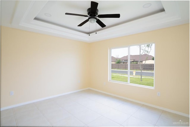 unfurnished room with light tile patterned floors, a tray ceiling, and ceiling fan