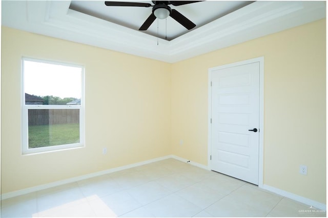 spare room featuring a tray ceiling, ceiling fan, and light tile patterned floors