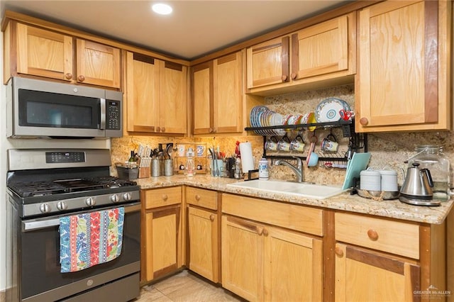 kitchen with light stone countertops, appliances with stainless steel finishes, backsplash, and a sink